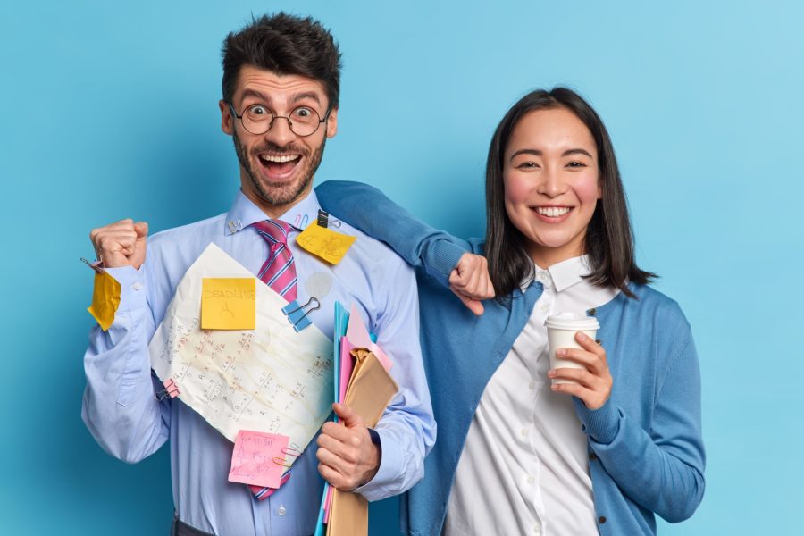 Successful businessman raises clenched fist and celebrates success at work female colleague stands n